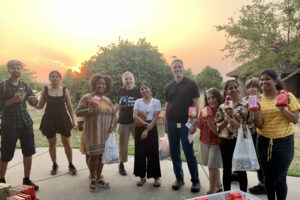 10 people + 1 child (behind) with Fair Trade products in their hands: Tony's Chocolonely, Peace Coffee, & Fair Trade tea in front of the setting sun