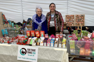 2 women stand behind a table. On the table: Fair Trade chocolate, coffee, & artisan products from Haiti